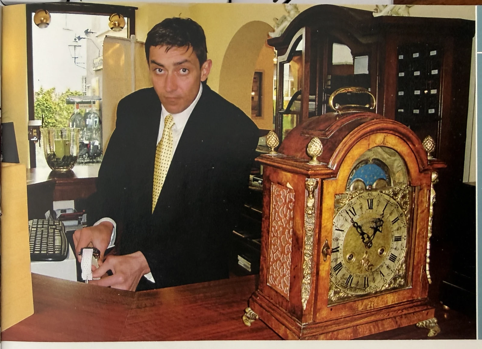 Eduard Weinbender im Atelier, neben einer antiken Bracket Clock mit Messingbeschlägen auf dem Tresen